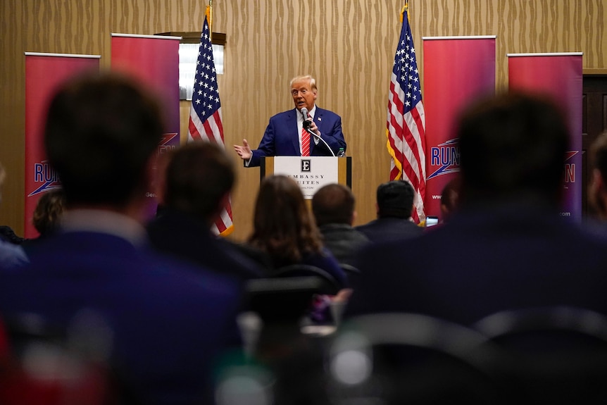 Donald Trump en el escenario de un mitin en Iowa, con dos banderas estadounidenses a su lado.