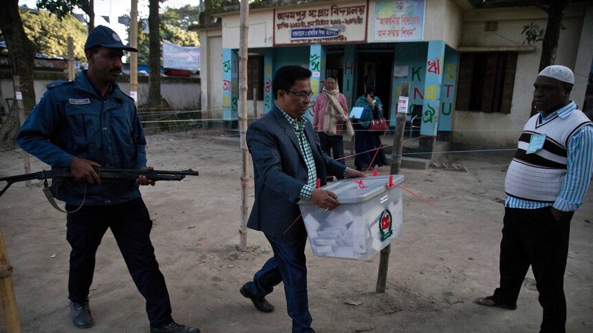 A Bangladeshi official carries a sealed ballot box flanked by security