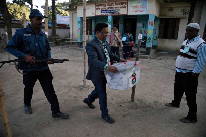 A Bangladeshi official carries a sealed ballot box flanked by security