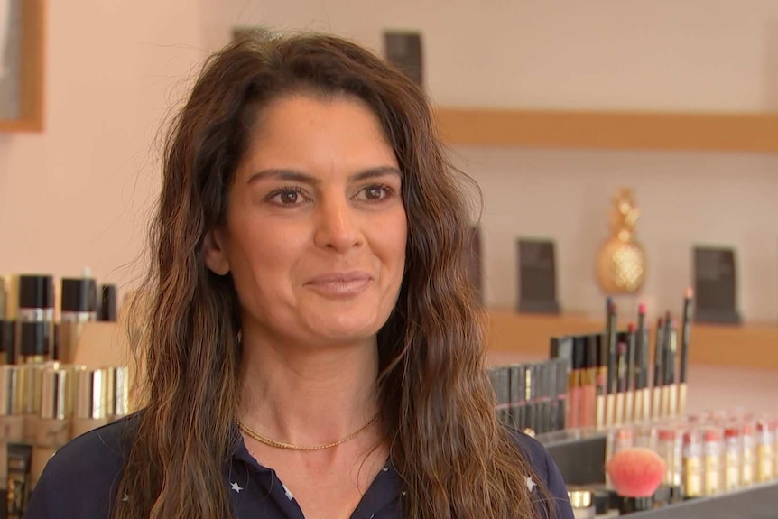 Melbourne beauty therapist Leanne Jones smiling in front of a rack of cosmetics.