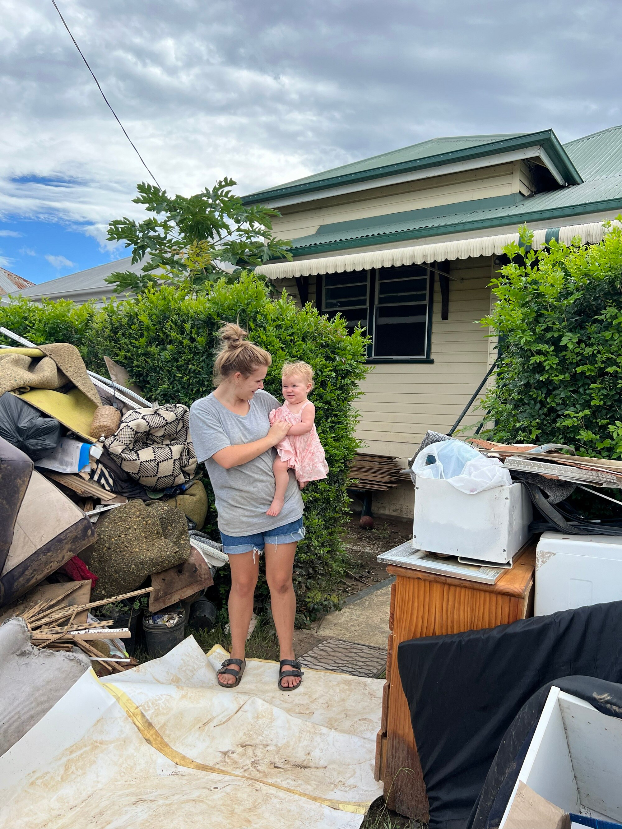 Uma mulher e sua filha estão do lado de fora de sua casa com pilhas de pertences danificados pela enchente.