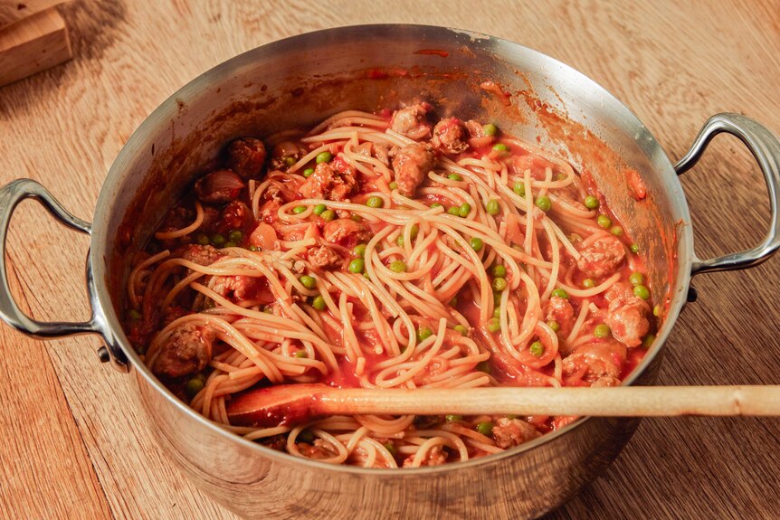 Fry pan filled with tomato and sausage spaghetti with peas, ready for a weeknight dinner.