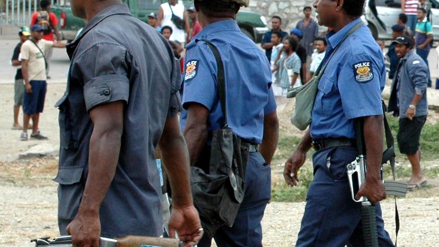 Armed Papua New Guinea police walk past an agitated crowd following a disturbance at Koki Market