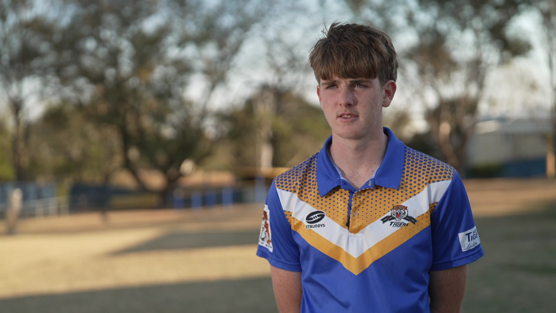 A boy wearing a blue, white and yellow polo shirt standing on a rugby league field.