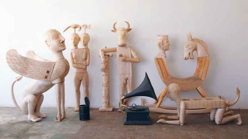 A collection of statues and carvings combining mythological beings and symbols with human limbs and a gramophone