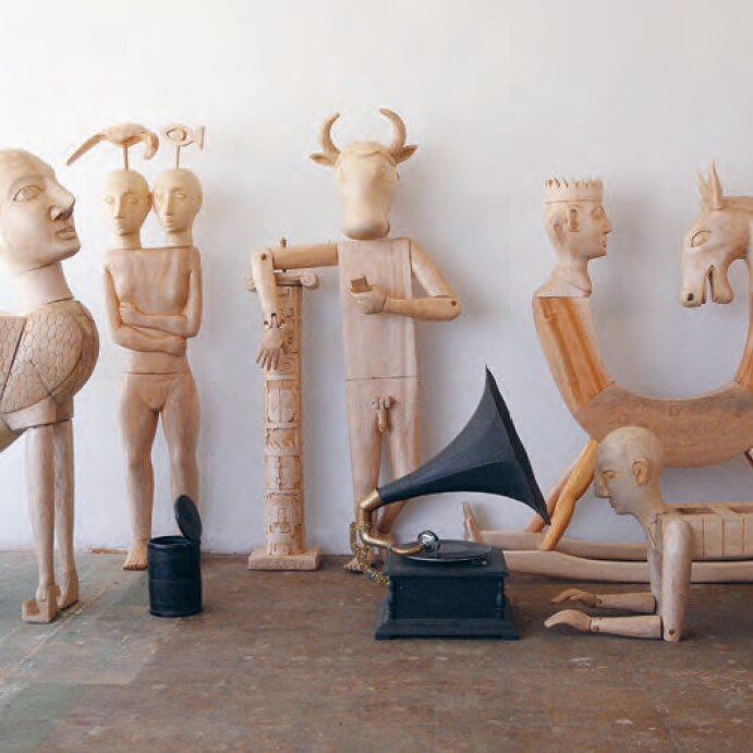 A collection of statues and carvings combining mythological beings and symbols with human limbs and a gramophone