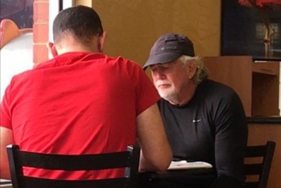 Two casually dressed men sit at a table in a Subway sandwich outlet.