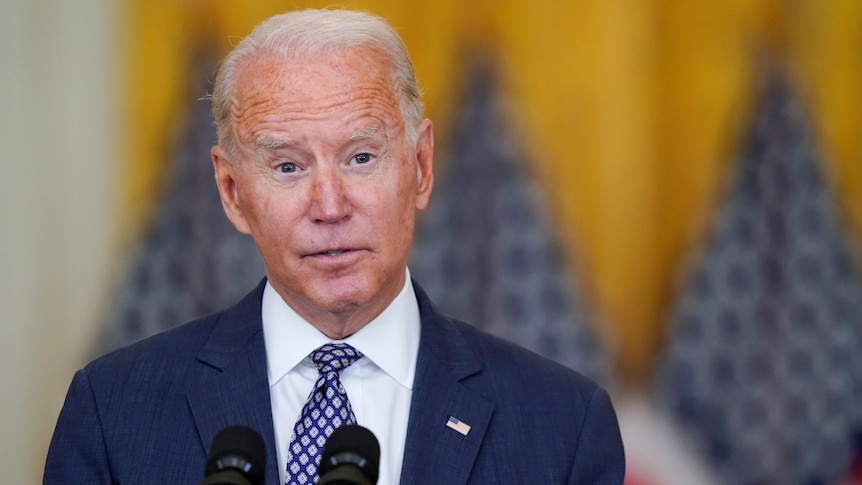 US President Joe Biden speaks while standing in front of several American flags