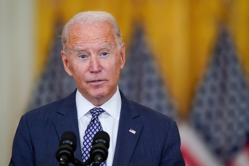 US President Joe Biden speaks while standing in front of several American flags