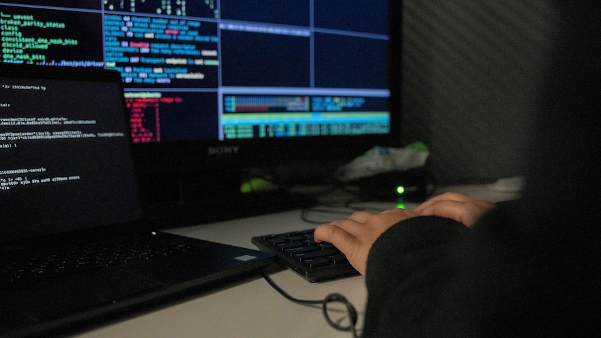 Unidentified person typing on computer keyboard in darkened room.