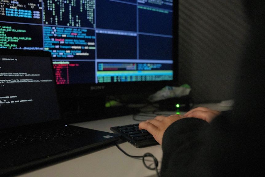 Unidentified person typing on computer keyboard in darkened room.