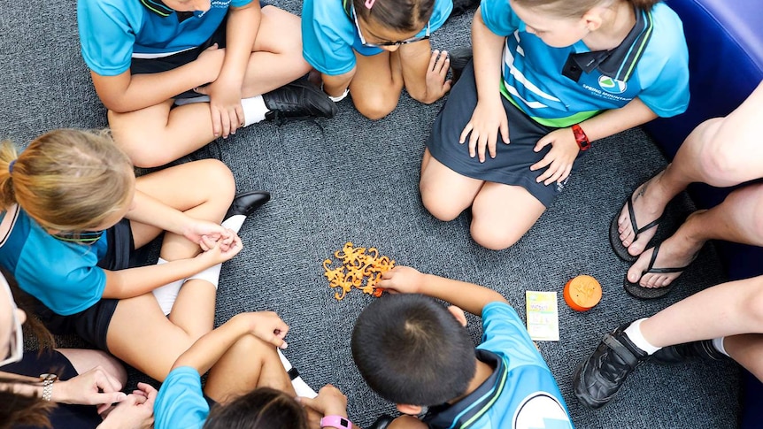 New prep-aged children sit on floor in circle in prep classroom playing barrel of monkeys game at Spring Mountain State School.