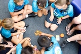 New prep-aged children sit on floor in circle in prep classroom playing barrel of monkeys game.