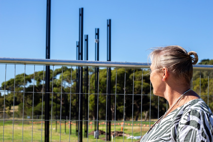 An older woman looks at a number of tall black metal poles which will form a fence at the edge of a baseball field