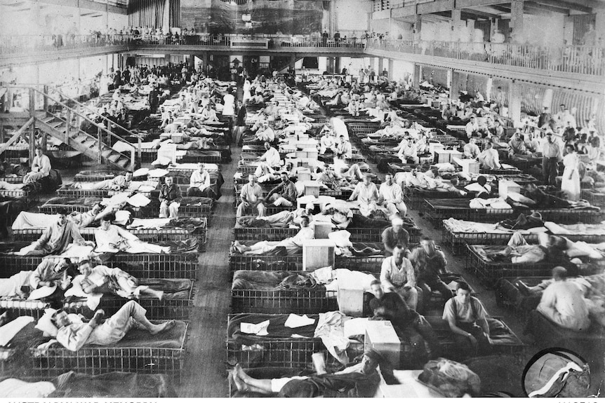Black and white image of a large room filled with five or more rows of beds and hundreds of wounded