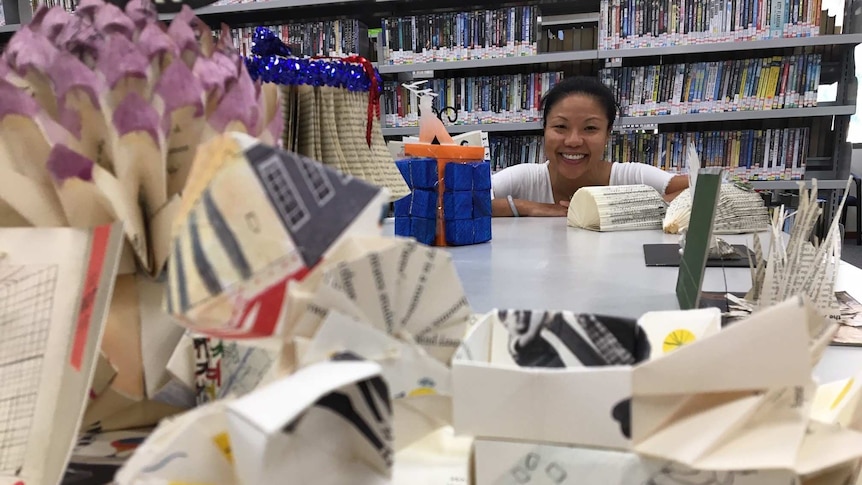A woman smiles while surrounded by paper crafted objects