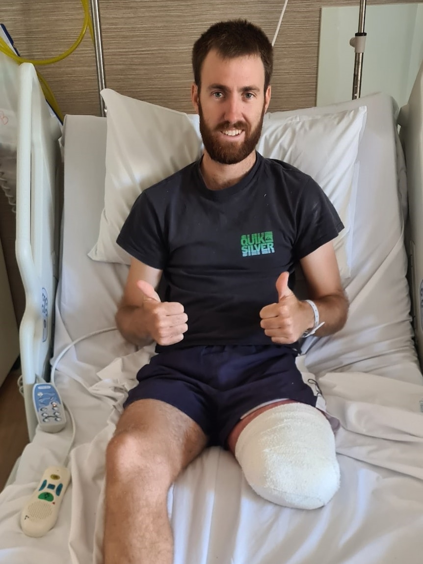 A man with a bandaged, amputated leg gives the camera a thumbs up sitting in his hospital bed