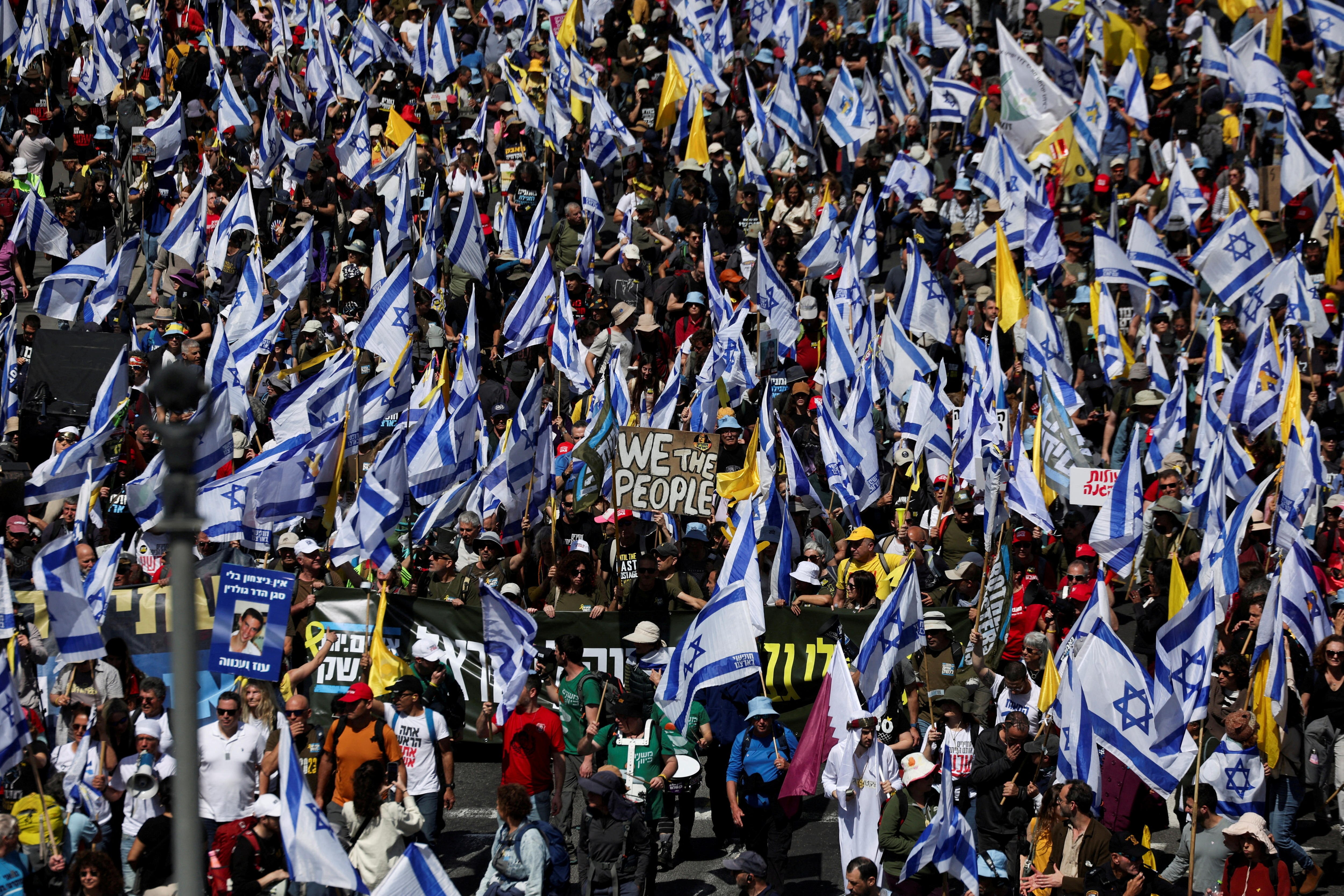 A huge crowd of protesters, many with Israeli flags, march along a road.