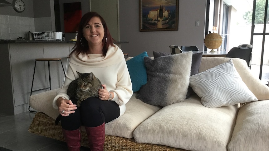 A woman sits with her cat on a couch.