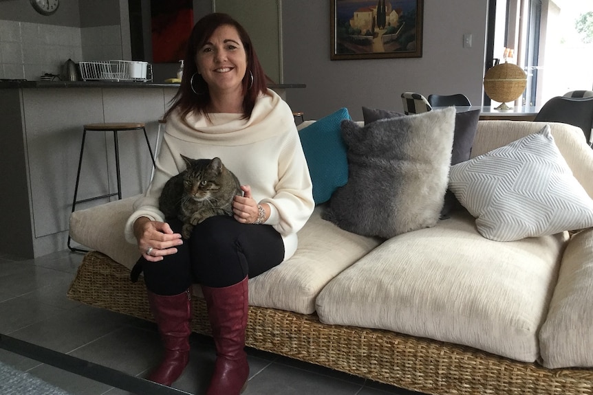 A woman sits with her cat on a couch.