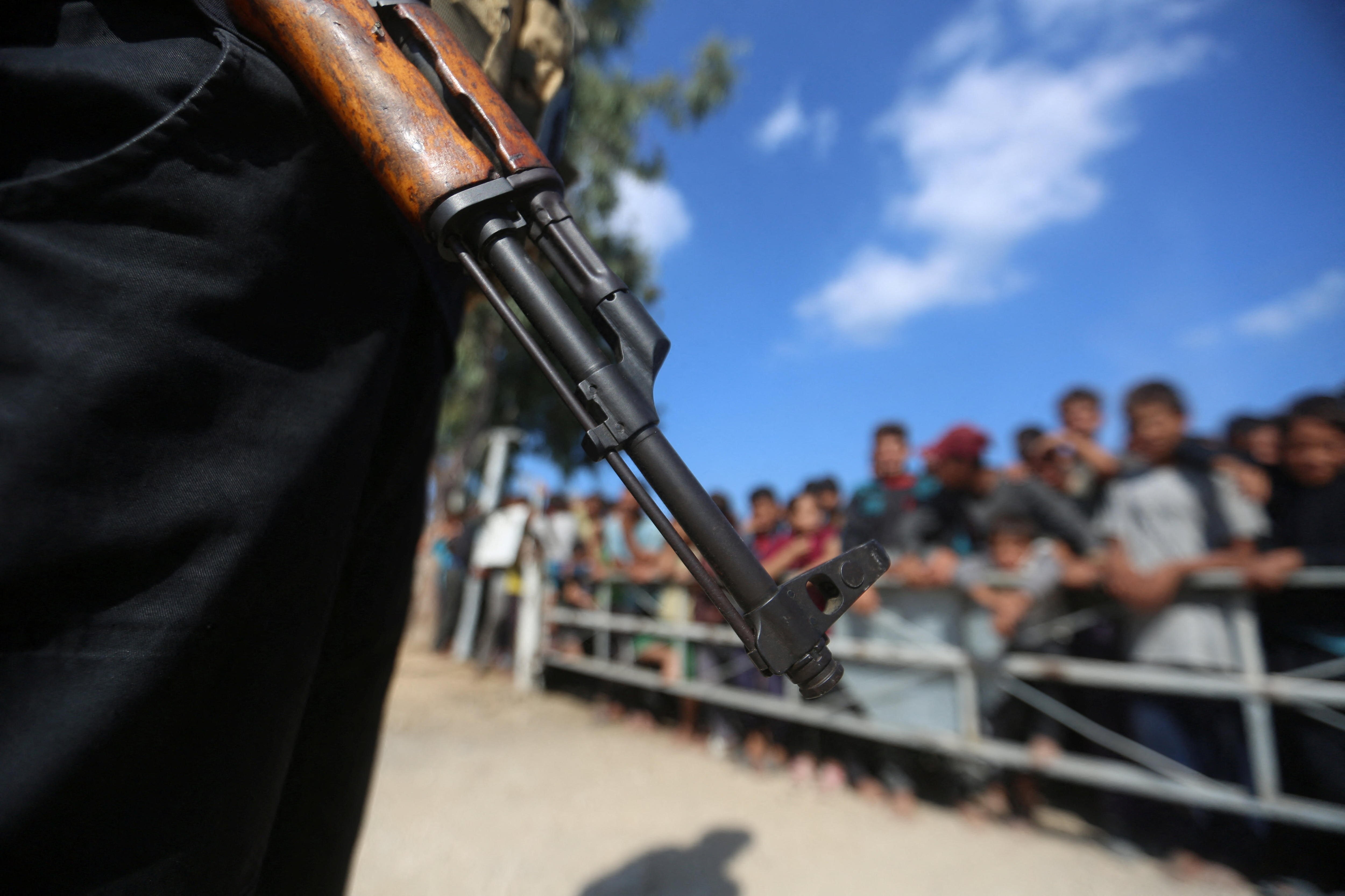 A close-up of a person holding a gun in the foreground with a crowd of people in the background.
