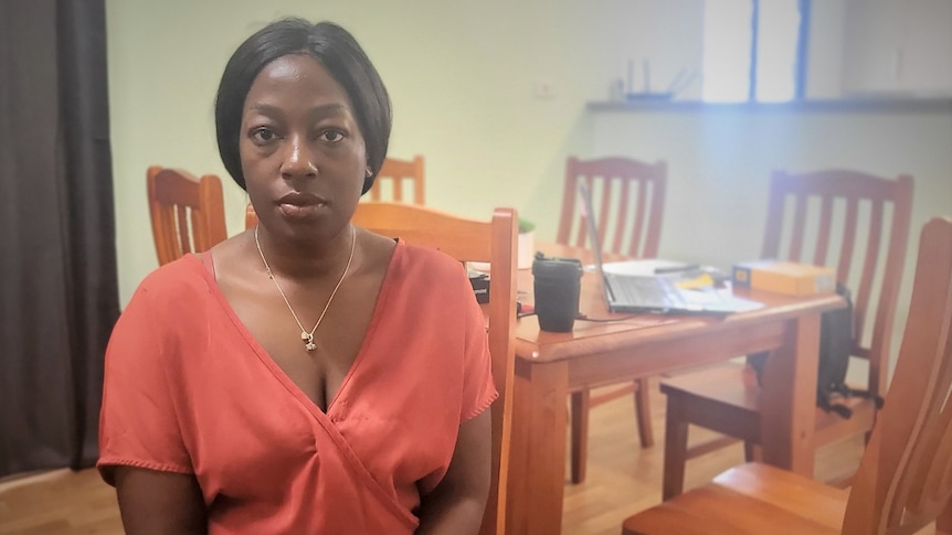 A woman looks seriously at the camera while sitting in a kitchen