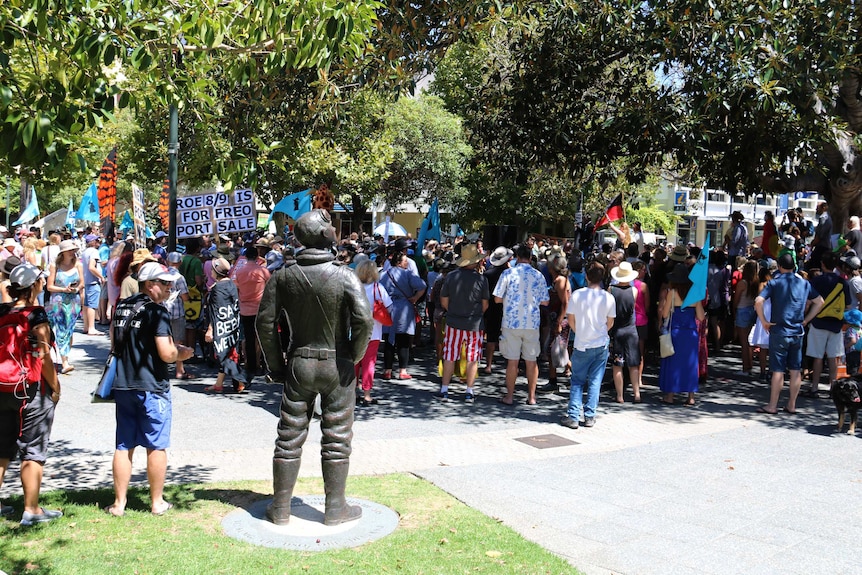 A crowd of people stands in Fremantle's Kings Square with some holding flags and signs.