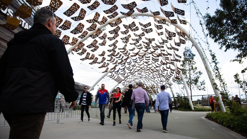 A small crowd of people walking under a walkway at Perth Stadium.