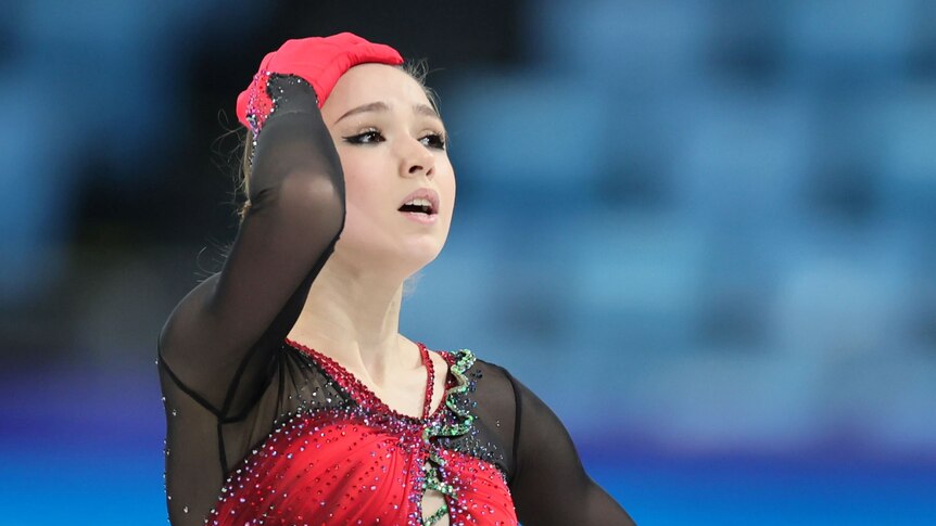 Russian figure skater Kamila Valieva puts her hand on her head while standing on the ice at the Winter Olympics.