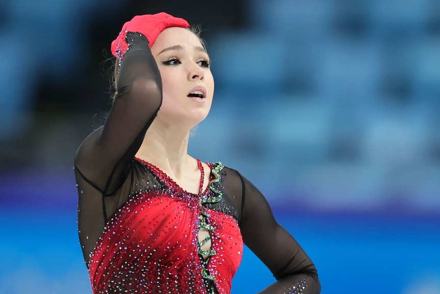Russian figure skater Kamila Valieva puts her hand on her head while standing on the ice at the Winter Olympics.