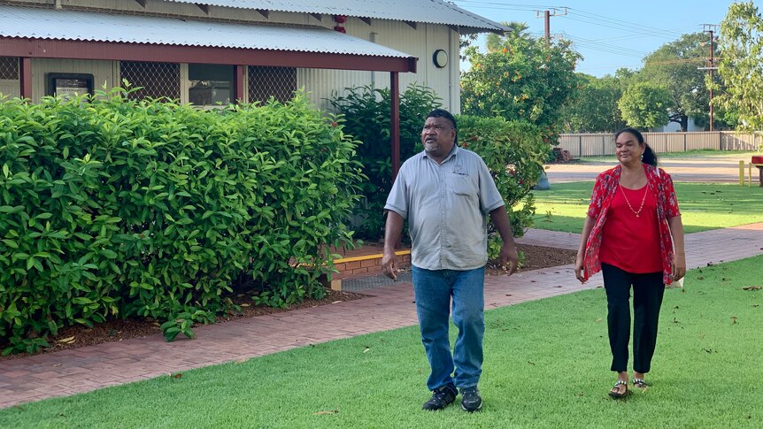 Two people walk on some grass near a building in northern Australia