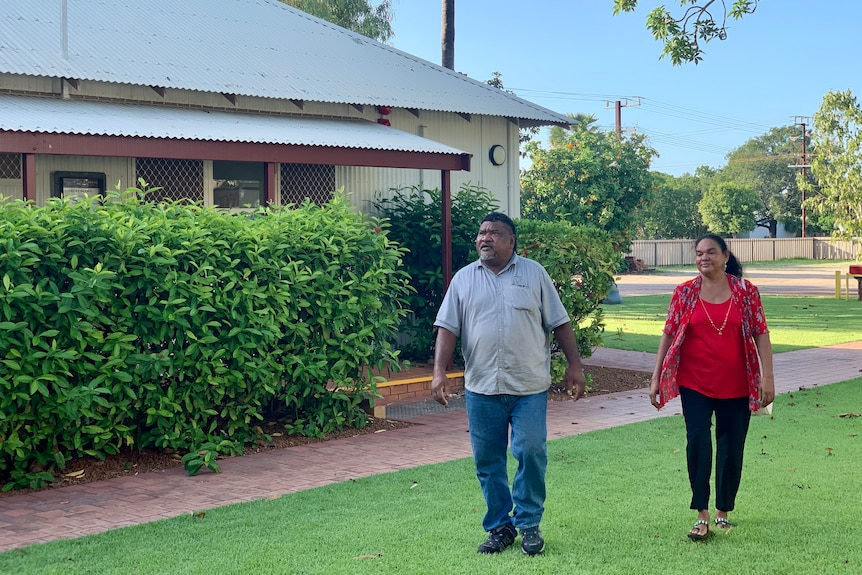 Two people walk on some grass near a building in northern Australia