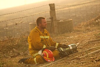 A firefighter sits next to hits helmet and air tank staring into the distance