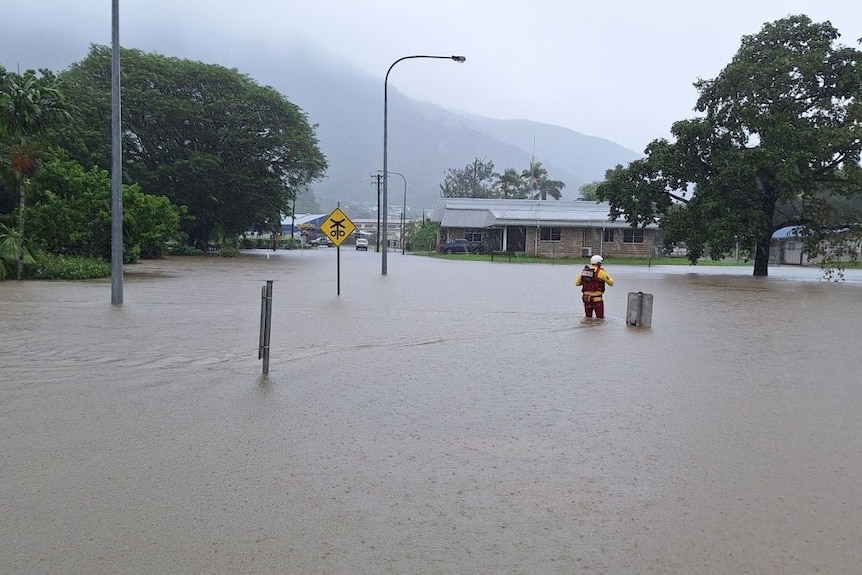 An emergency services worker stands in a flooded road.