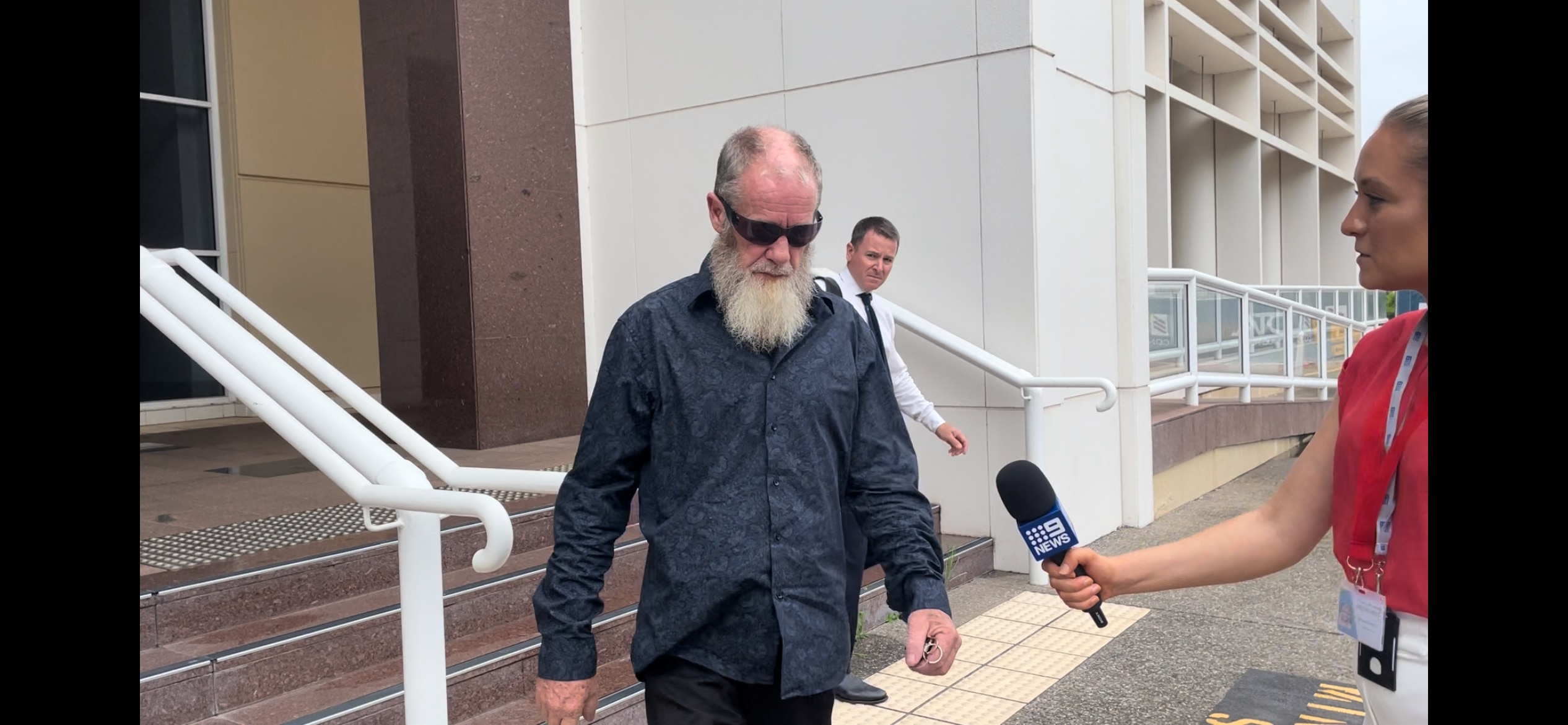 A middle-aged man with a beard walks out of a court house 