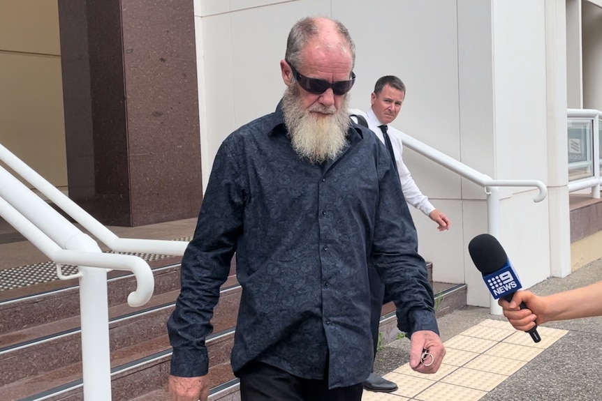 A middle-aged man with a beard walks out of a court house 