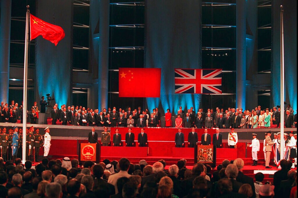 Among a crowd, you look up at a stage with Chinese and British dignitaries as British soldiers lower the Union Jack.