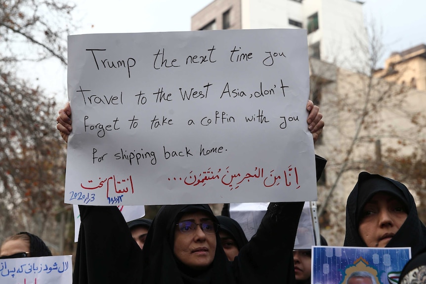 Woman in black head scarf holds a protest sign above her head.