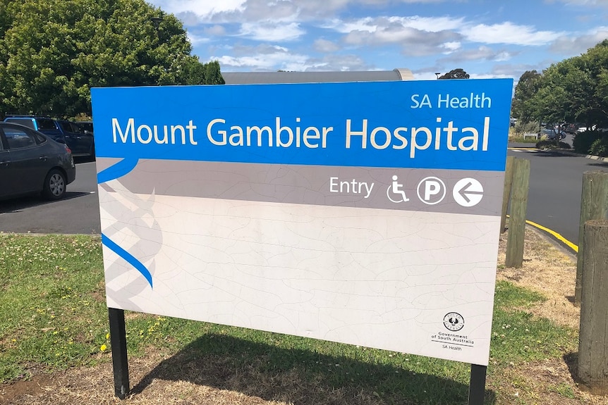 A blue and white sign that reads "Mount Gambier Hospital" standing in front of a carpark.