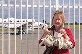 A woman wearing red smiling and holding the christmas pudding standing next to the plane.