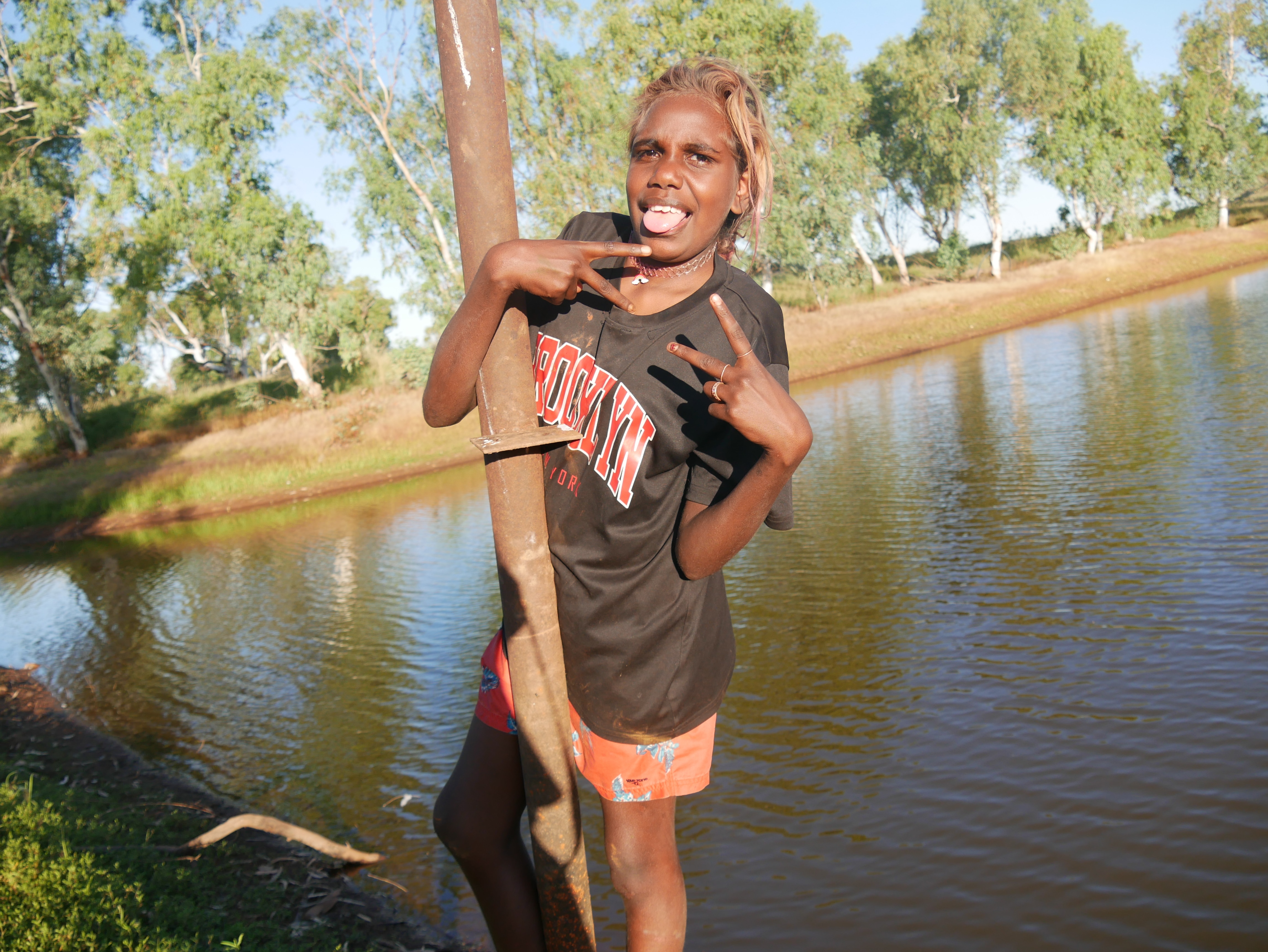A teenager in Balgo poses with her hands in piece signs near the dam.