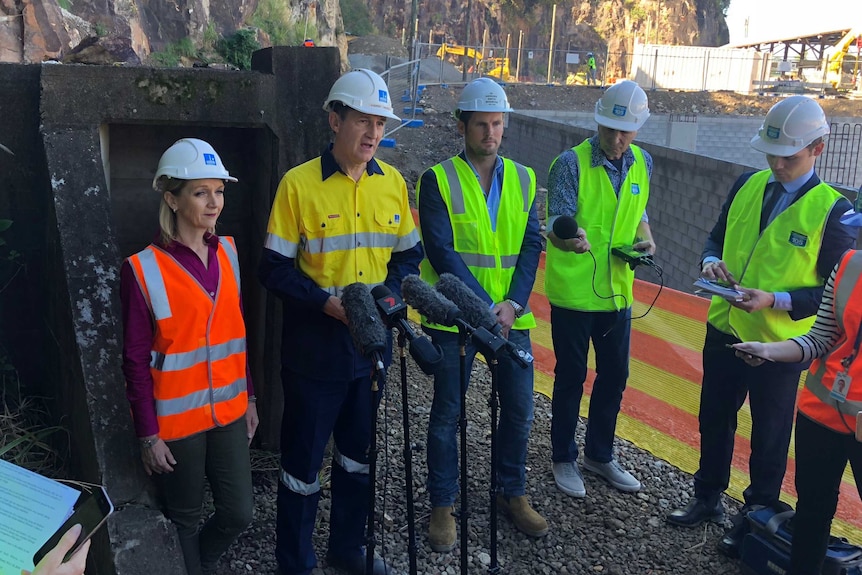 People in hard hats and high-vis vests talk to media