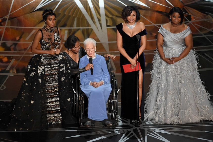 Katherine Johnson sits in a wheelchair on stage with the female cast of Hidden Figures at the Oscars
