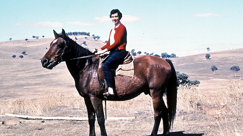 A film photo of a teenage girl sitting on a brown horse, with rolling brown hills and trees in the background.
