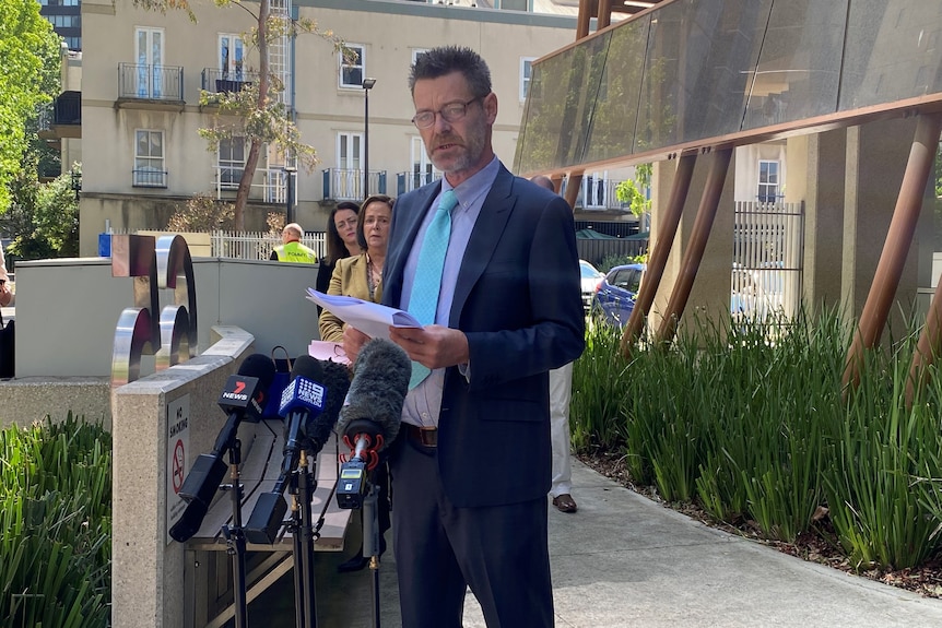 Richard Hickey wears a dark suit, blue shirt and tie and reads a statement outside court.