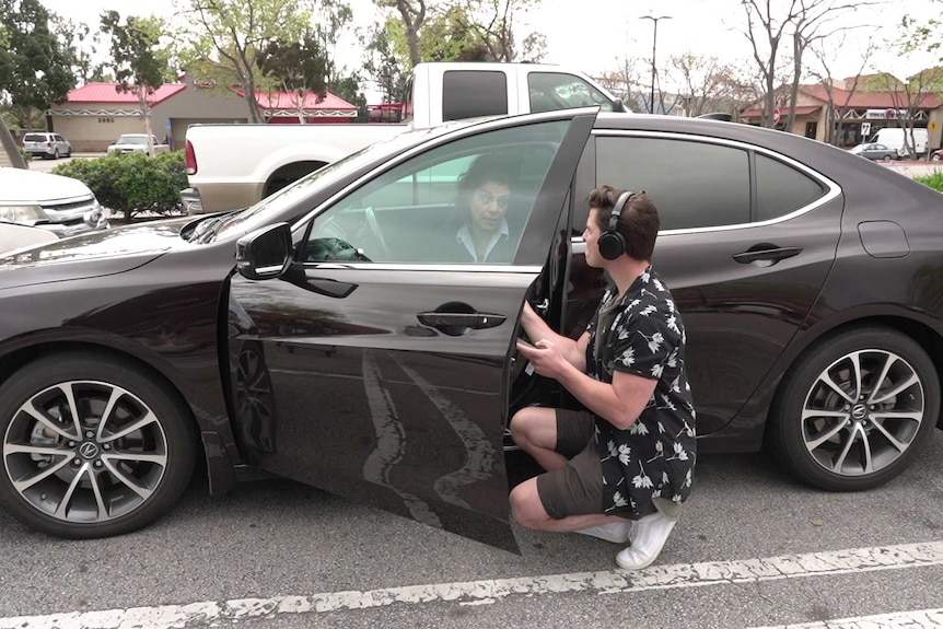 A man with recording gear crouching inside a car door.