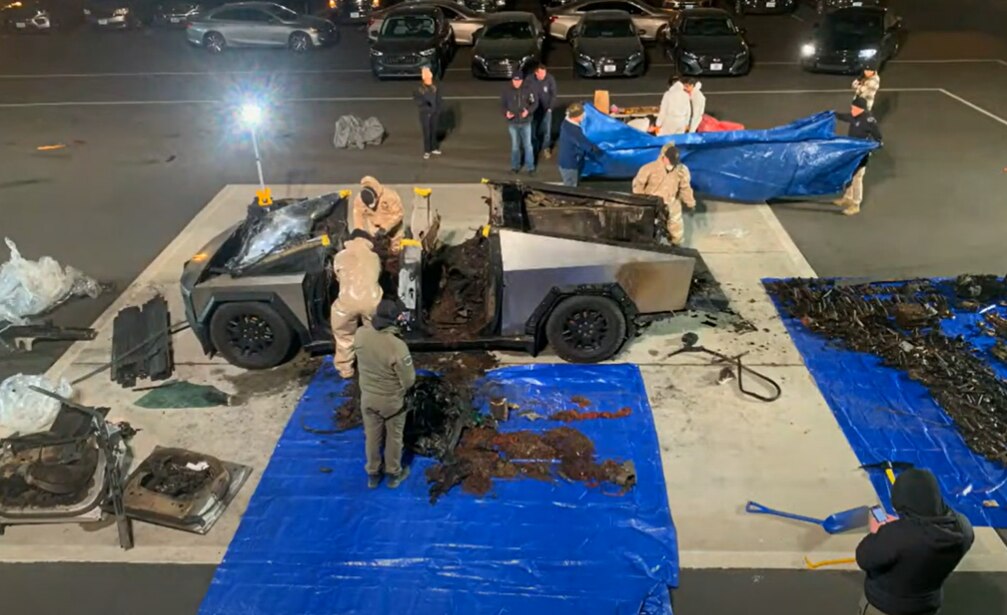 People stand around an exploded cybertruck surrounded by blue tarps containing debris 