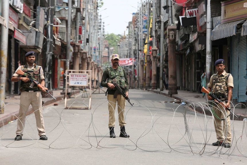 Three armed officers standing behind barbed wire