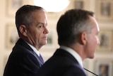 Bill Shorten looks at Chris Bowen, who is only seen from behind. Mr Shorten is wearing a navy suit and purple tie.