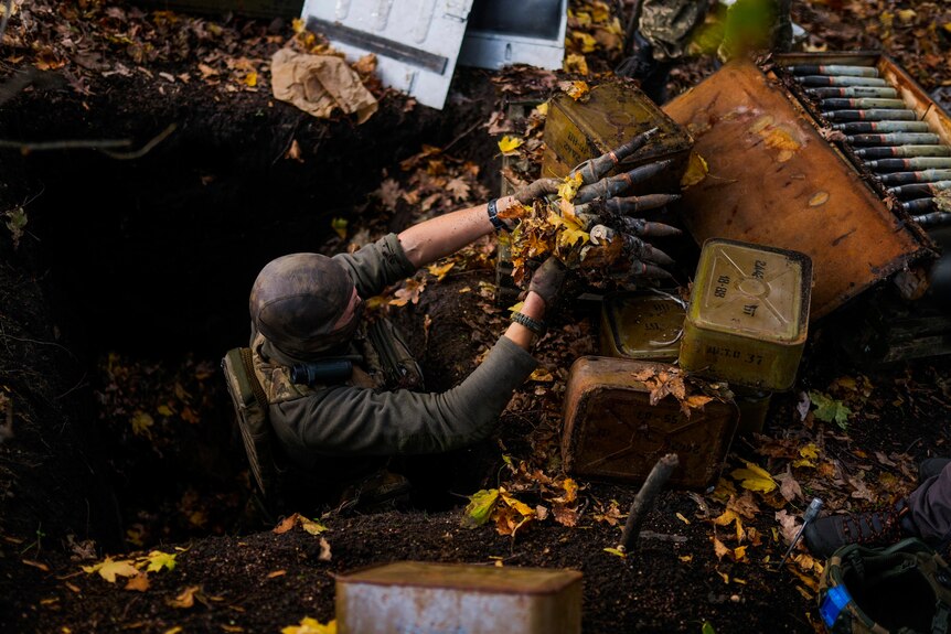 A man takes ammunition out of a hole and places it on the ground